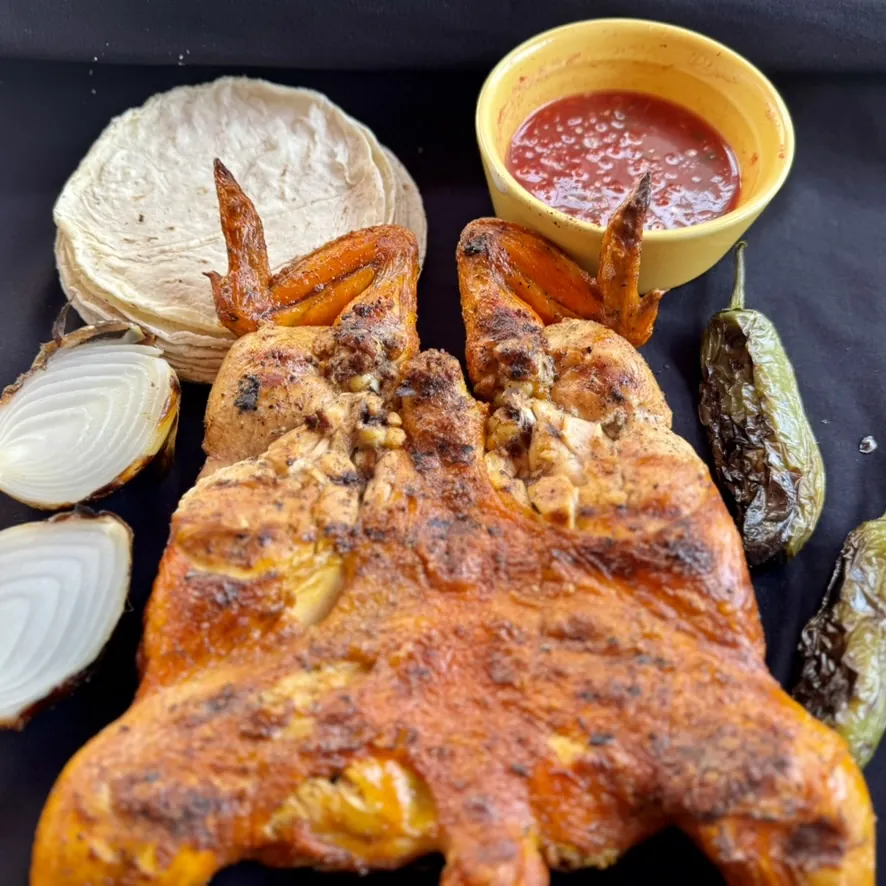Pollo entero asado al carbón de El Pollo, con tortillas, salsa roja, cebolla y chiles asados